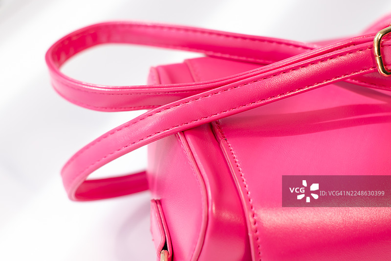 特写镜头下，一个带有手柄的鲜艳粉色钱包，背景为纯净的白色，突出了其质感和设计。图片素材