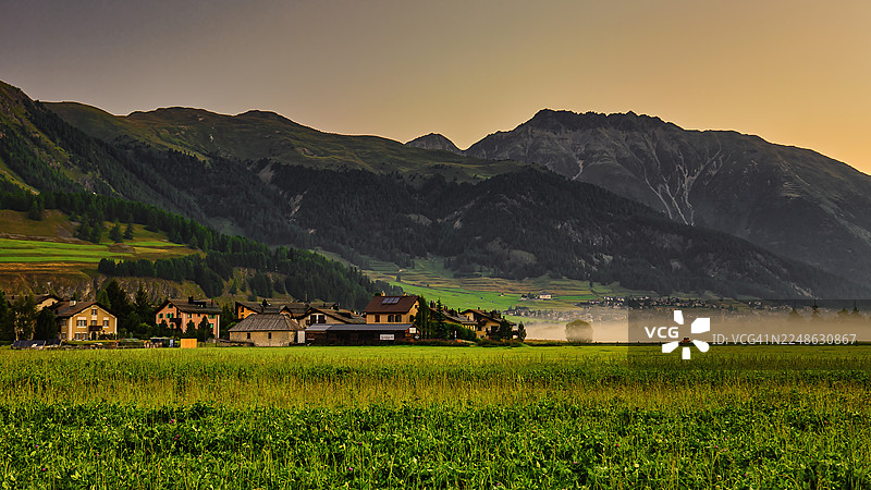 日出时分，如画的山村坐落在郁郁葱葱的山谷中，田野间升腾着薄雾，瑞士锡尔瓦普拉纳图片素材
