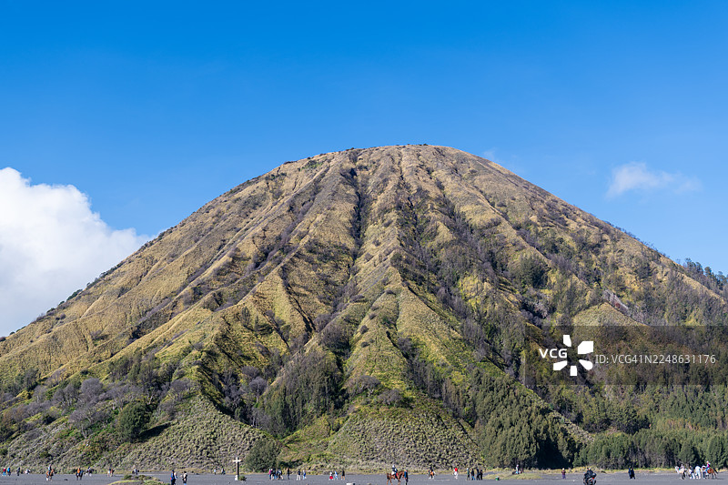 在湛蓝的天空下，大山脚下有游客和马匹，展现了自然的广阔与冒险精神图片素材