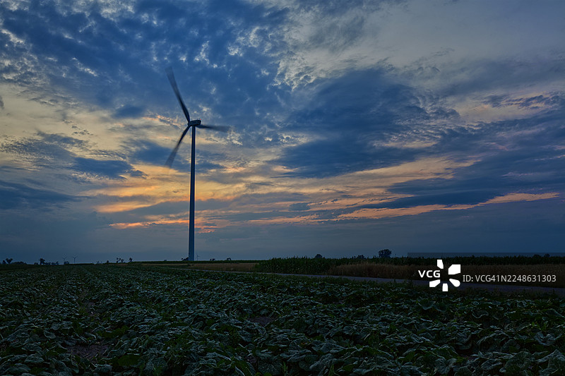 傍晚时分田野里的风力发电机，在充满云彩的天空中展示的可再生能源美景，波兰，桑尼基图片素材