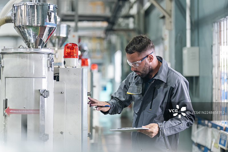 工厂里，技术人员正在操作塑料注塑机的控制面板。图片素材