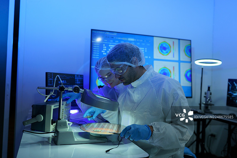 国际男女技术人员身穿无菌服，在半导体制造厂使用显微镜工作图片素材