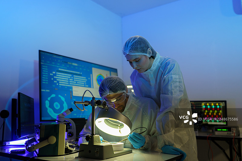 国际男女技术人员身穿无菌服，在半导体制造厂使用显微镜工作图片素材