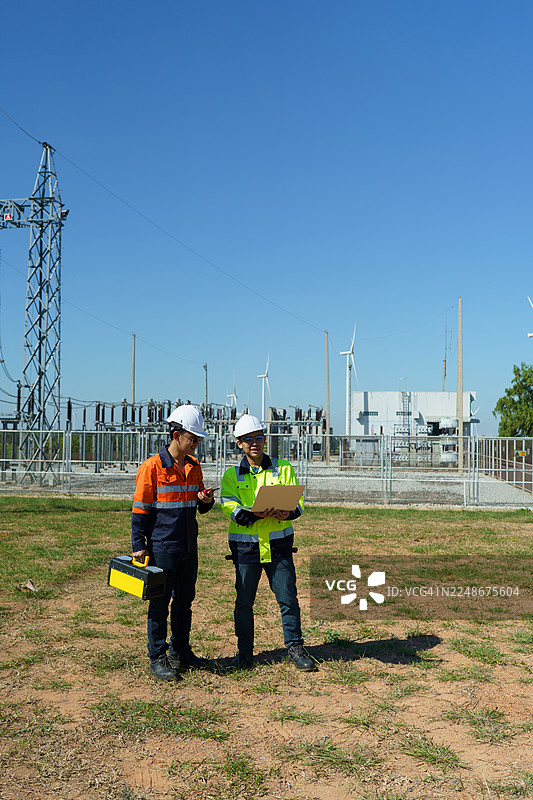 工程师正在检查大型风力涡轮机的运行情况，该涡轮机正在风力发电场中发电。图片素材