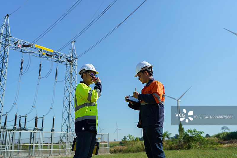 工程师正在检查一座大型风力涡轮机的工作情况，该涡轮机正在风电场中发电。图片素材