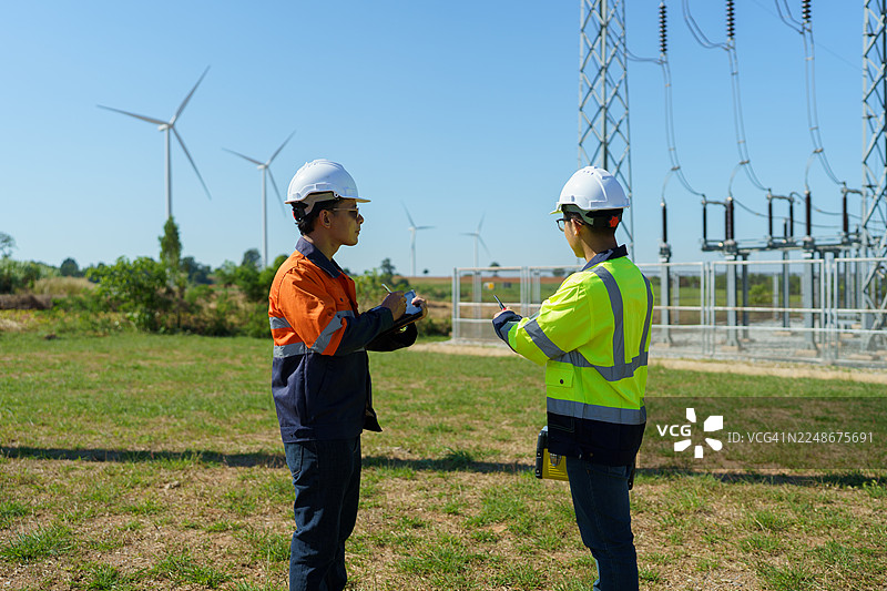 工程师正在检查一座大型风力涡轮机的运行情况，该涡轮机正在风力发电场中发电。图片素材