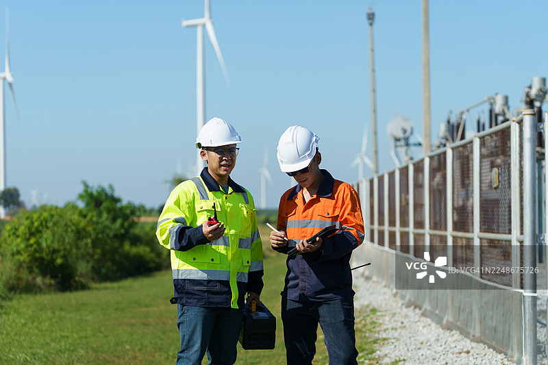 工程师正在检查一座大型风力涡轮机的运行情况，该涡轮机正在风电场中发电。图片素材
