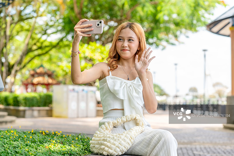 亚洲Z世代女性在古晋滨海公园自拍。年轻的亚洲女性在砂拉越河畔户外微笑着用手机。图片素材