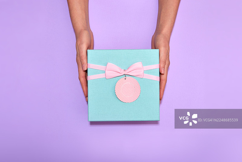 一只手拿着一个带有粉色蝴蝶结的绿松石色礼品盒图片素材