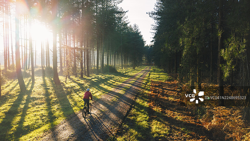 航拍视角下，一位成熟的男士在阳光明媚的秋日早晨，骑着砂石公路车探索森林。图片素材