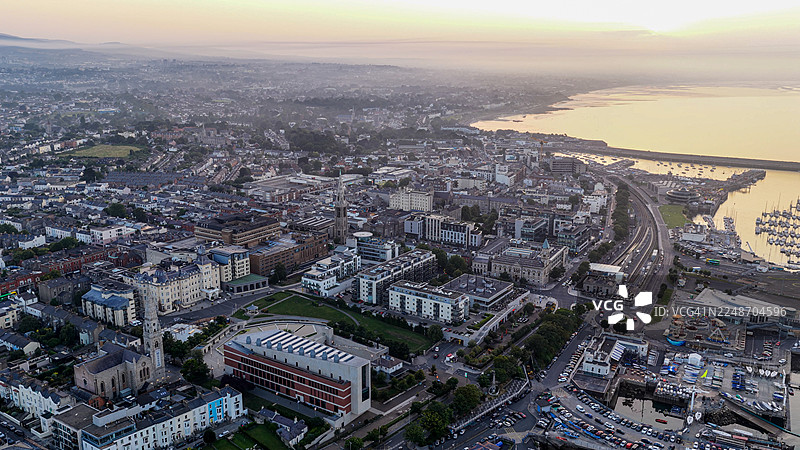 日落时分邓莱里港和码头的鸟瞰图,都柏林海岸小镇,有船只、码头和海滨建筑,爱尔兰海滨风景,海面平静,天空发光,旅行和旅游概念,适用于社论和设计用途图片素材