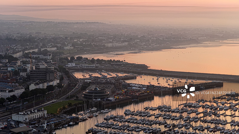 日落时分的邓莱里港和码头的鸟瞰图，都柏林沿海小镇，有船只、码头和海滨建筑，爱尔兰海滨风光，海面平静，天空发光，旅行和旅游概念，适用于社论和设计图片素材