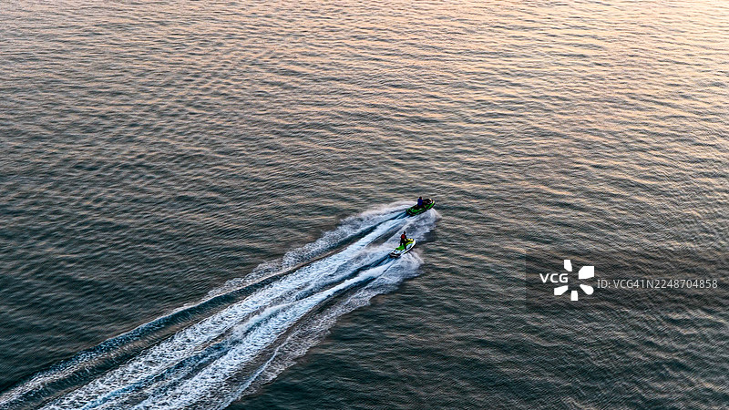 日落时分，都柏林爱尔兰邓莱里港平静的海面上，船只、摩托艇和划手在空中俯瞰，金色的倒影映照在海面上，展现了海上活动、沿海旅行和休闲的概念，适用于爱尔兰海滨设计。图片素材