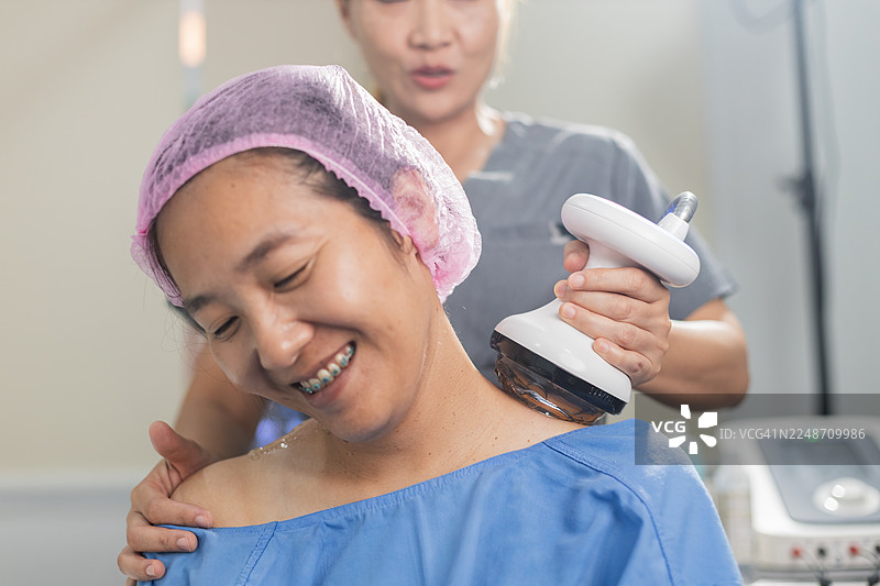 理疗师用冲击波治疗仪为女性患者的肩膀进行治疗，代表现代办公室综合征的治疗图片素材