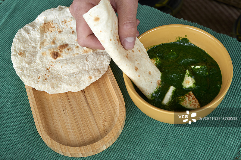 人的手将恰巴提浸入印度菠菜奶酪咖喱图片素材