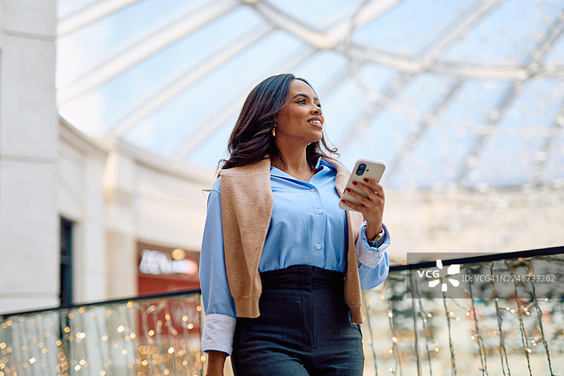 年轻女子在现代商场购物时使用智能手机，享受生活与科技图片素材