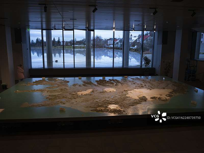 雷克雅未克市政厅内展示的冰岛地图，窗外是冰封的泰宁湖，一位游客正在观看冰岛地图图片素材