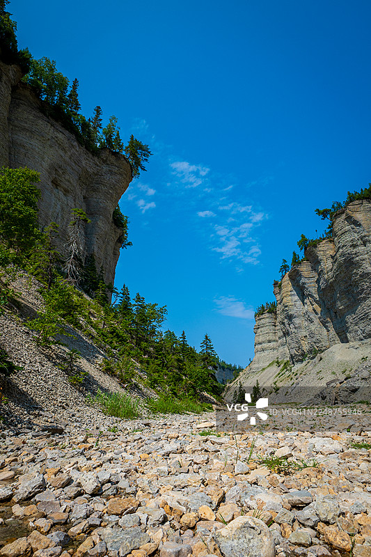加拿大魁北克省安提科斯蒂岛，瓦洛里瀑布附近，晴天下的湛蓝天空下，是陡峭的峡谷、石崖、浅滩河流、坠落的巨石和北方森林。图片素材