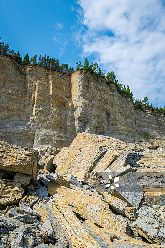 夏季光线下层叠的岩石、断裂的巨石、矿物纹理和沉积岩悬崖，靠近加拿大魁北克省安蒂科斯蒂岛的沃罗尔瀑布图片素材