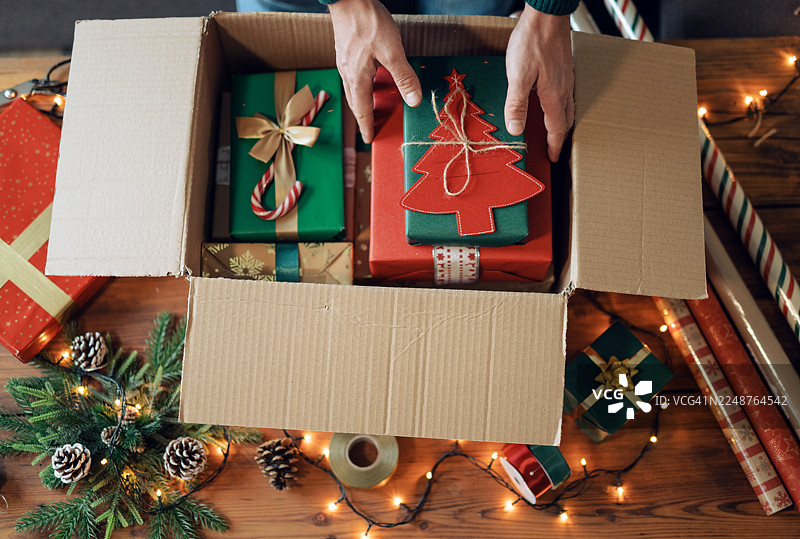 男人正在准备圣诞礼物，将它们装入纸箱中准备寄出。图片素材