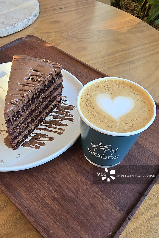 木桌上摆放着一块美味的巧克力蛋糕，旁边是一杯带有拉花艺术的咖啡，是享受甜蜜时刻的绝佳选择图片素材