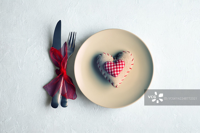 餐桌上餐具上心形图案的俯视照片，餐具用红丝带系住，象征着爱与庆祝图片素材