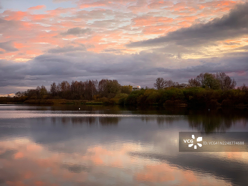 日落时分，宁静的湖面倒映着粉橙色云彩的壮丽天空，远处的树线勾勒出轮廓，爱沙尼亚塔尔图市伊哈斯特大道 T图片素材