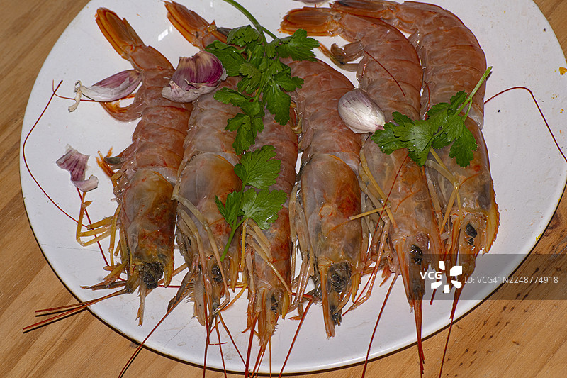 新鲜捕捞的大虾放在白盘中，配有大蒜和欧芹，准备烹饪图片素材