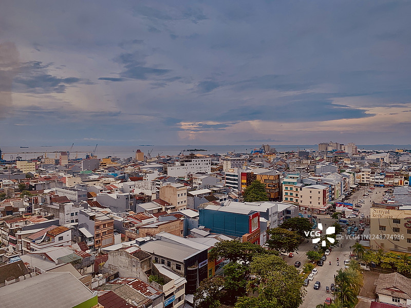 高角度俯瞰繁华的城镇，建筑和道路延伸至海边，天空布满云彩，印尼望加锡，RS Akademis Jaury Jusuf Putera图片素材