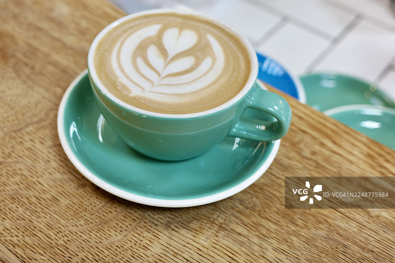 俯视角度拍摄的卡布奇诺咖啡，木桌上的拿铁艺术，鲜艳的青色杯子和碟子图片素材