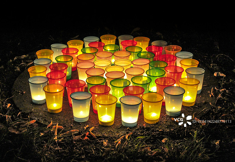 夜间地面上彩色塑料杯中点亮的茶蜡的高角度视图图片素材