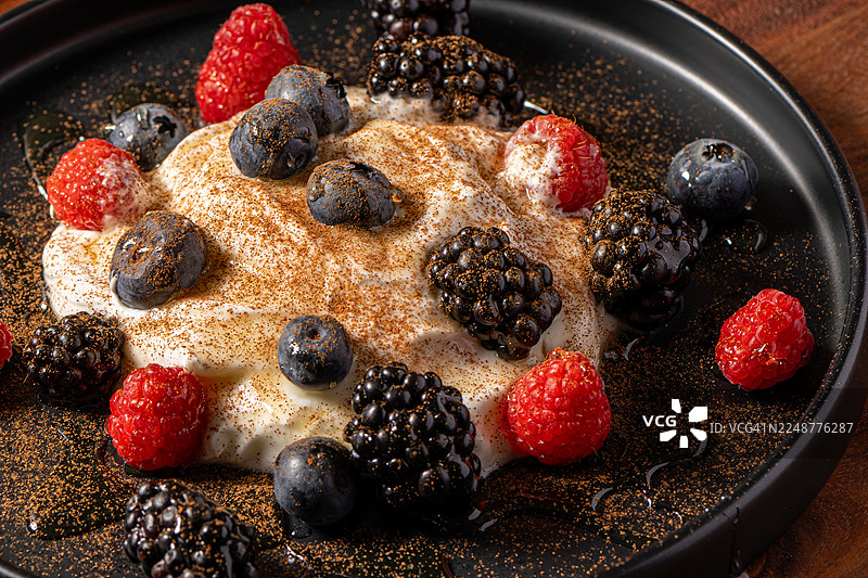 深色盘子上新鲜混合莓果和酸奶甜点的特写，撒上肉桂粉图片素材