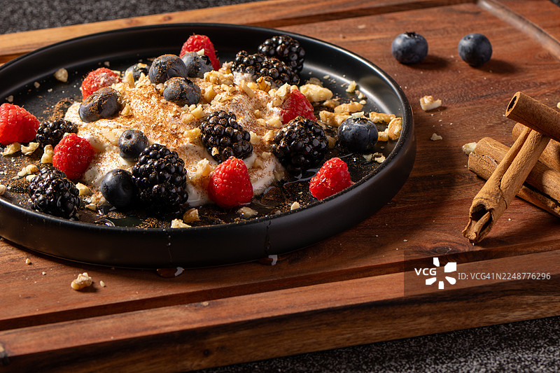 木桌上盛放着美味的早餐碗，里面有新鲜的浆果、坚果和酸奶，并用肉桂棒装饰。图片素材