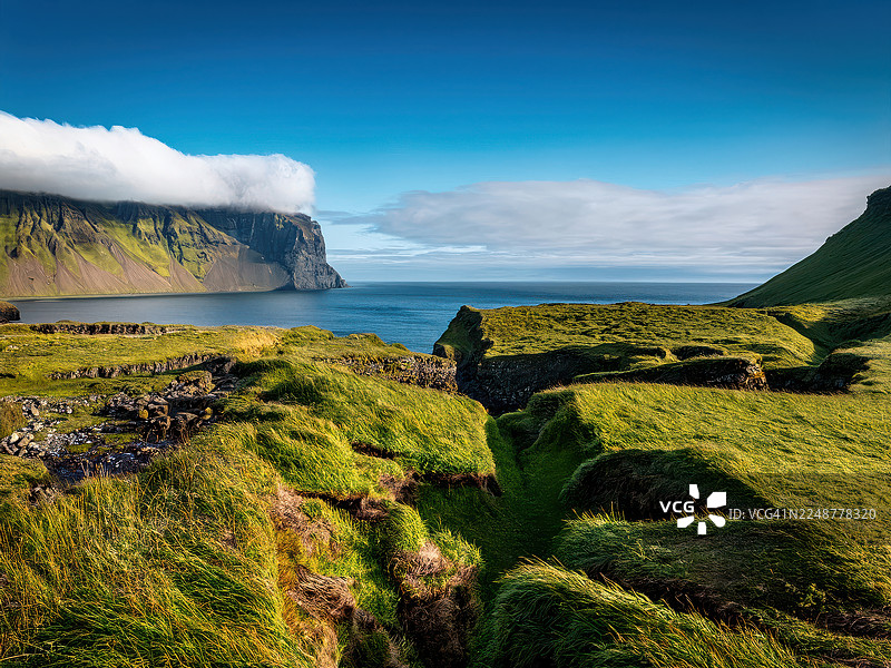 爱尔兰霍恩斯特兰迪尔自然保护区，海边悬崖和绿色的山峰，山顶被云雾笼罩，头顶是湛蓝的天空图片素材