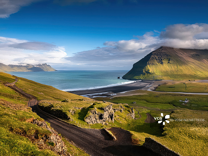 冰岛霍恩斯特兰迪尔自然保护区，绿色山丘、黑沙滩和山脉下的戏剧性海岸风光，蓝天白云图片素材