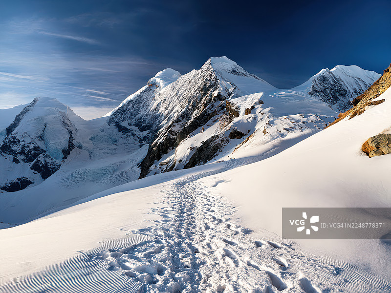 瑞士，小屋，晴朗蓝天下雄伟的雪山，雪地上的脚印引路图片素材