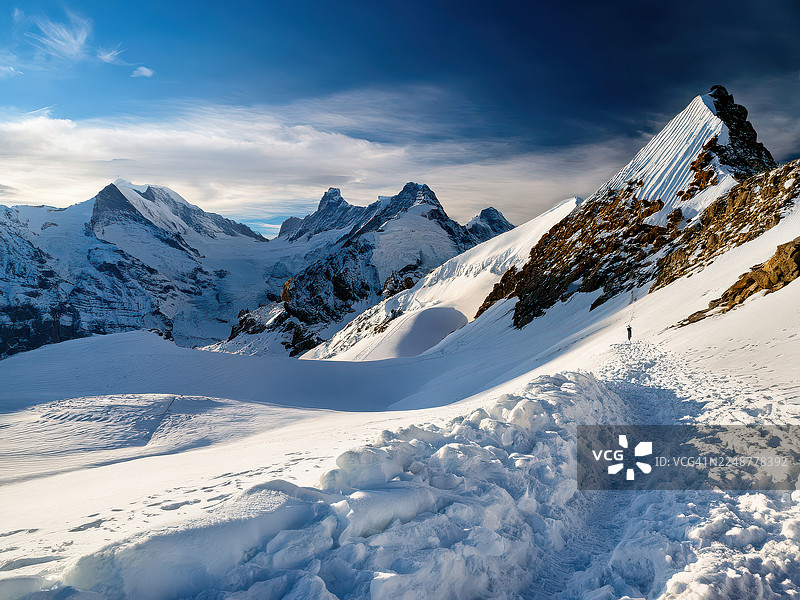 瑞士，小屋，在戏剧性的蓝天下，雄伟的雪山和冰川，一个人走在雪路上图片素材