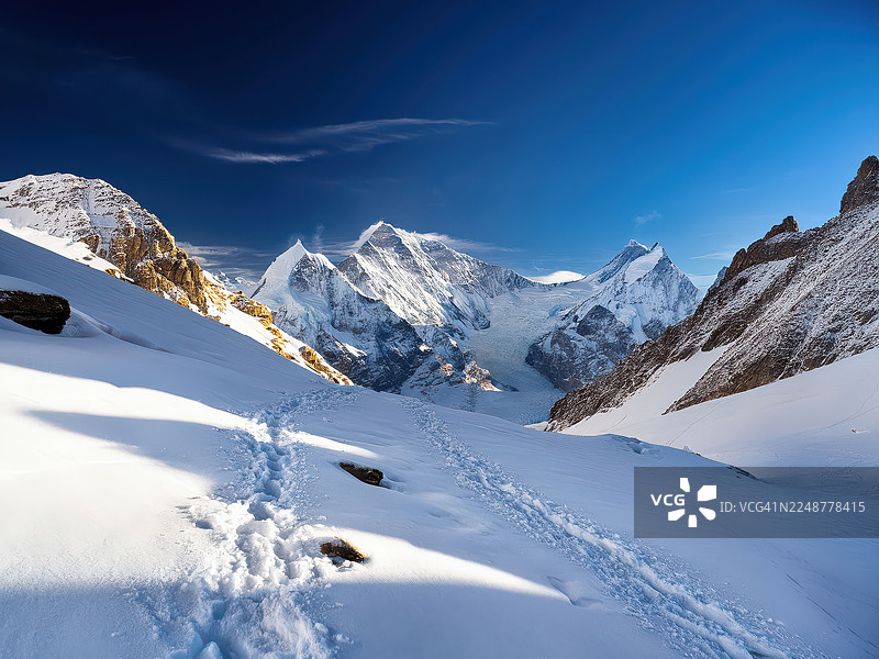 瑞士壮丽的雪山风光，蓝天白云下的 pristine snow，脚印蜿蜒其中，小屋点缀其间图片素材