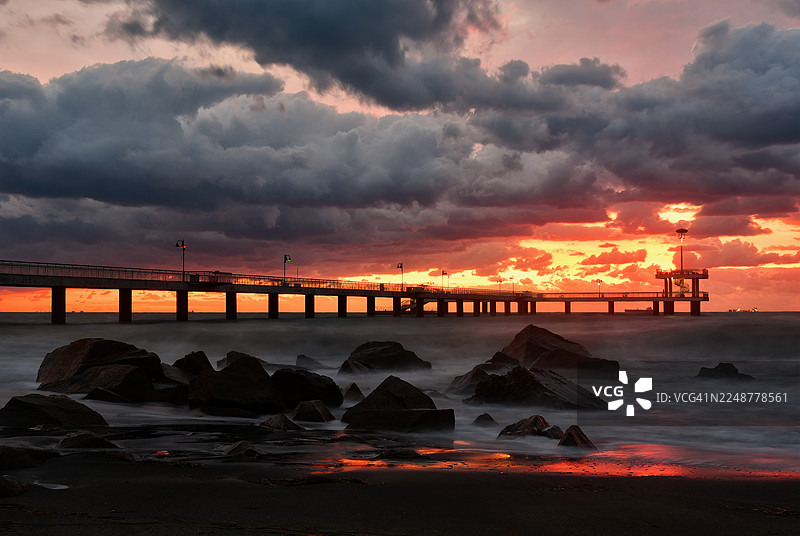 保加利亚布尔加斯，风暴般的天空下，长曝光下的水面营造出宁静而又充满力量的海滨景象，夕阳下的码头景象壮丽图片素材