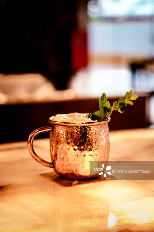 特写一杯清爽的饮品，盛放在铜杯中，饰以薄荷叶，置于木桌上图片素材
