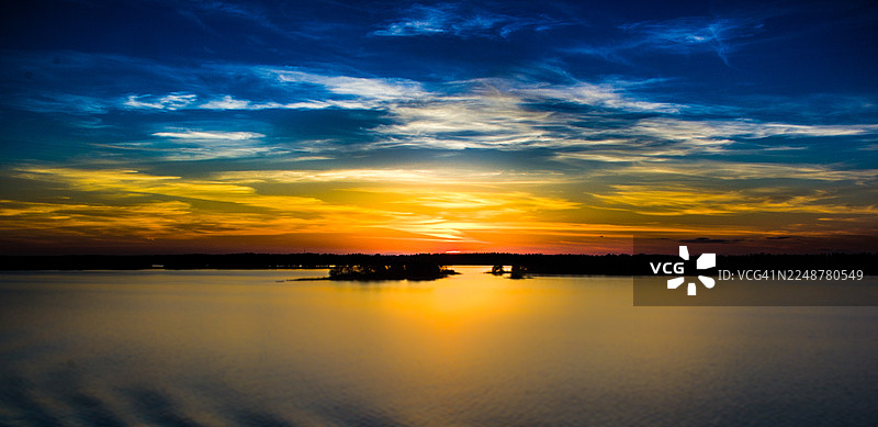 瑞典，宁静湖泊上生机勃勃的日落，树木剪影与湖面上的倒影，瑞典图片素材