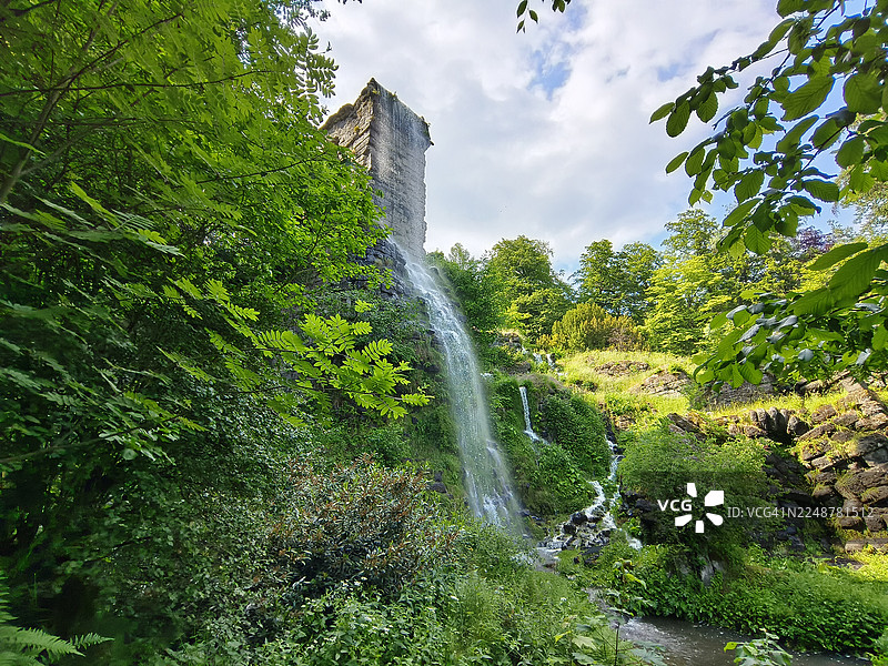 德国卡塞尔，云层密布的天空下，瀑布从茂密的绿色森林中倾泻而下，雄伟的低角度视角图片素材