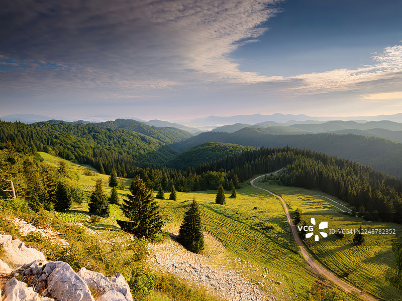 日出时分，蜿蜒的土路穿过克罗地亚戈尔斯基科塔尔生机勃勃的绿色山景图片素材
