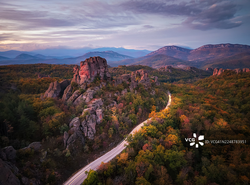 保加利亚，别尔格拉德契克，黄昏时分，多云天空下，具有戏剧性岩石构造的秋季森林景观中的蜿蜒道路图片素材