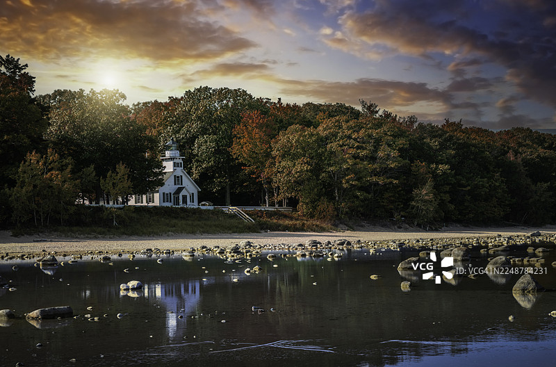 秋日落叶季，林荫海岸灯塔在湖面投下倒影，晚霞壮丽，美国特拉弗斯城图片素材