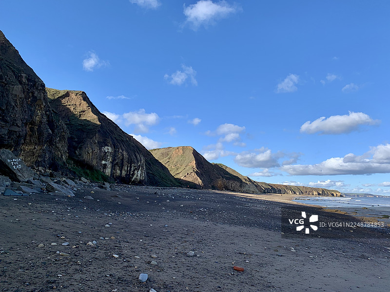 英国哈特尔浦崎岖的海岸线，拥有深色沙滩、陡峭悬崖，上方是部分多云的蓝天，英格兰海岸小径图片素材