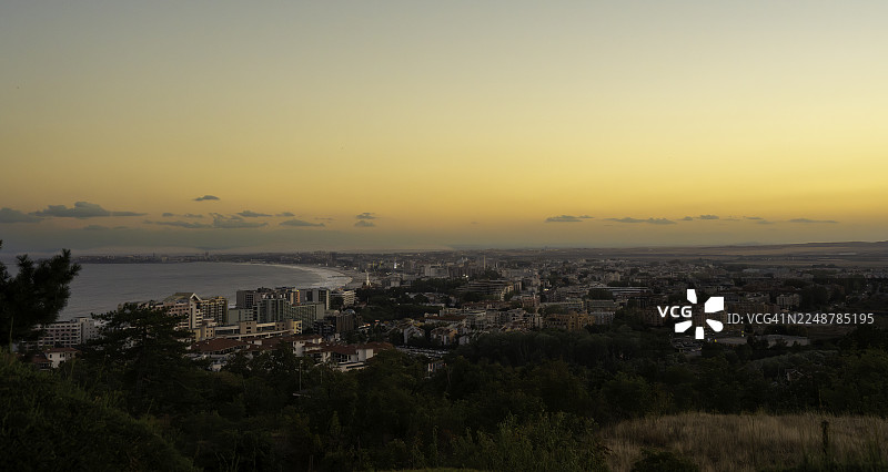 保加利亚Sunny Beach，高角度俯瞰海滨城镇，背景是生机勃勃的日落天空，大海和城市建筑沐浴在温暖的光辉中。图片素材