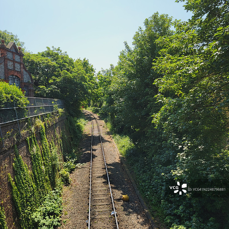 晴朗的蓝天下，阳光明媚，高角度俯瞰着穿过茂密绿树的铁轨和一座砖砌建筑。图片素材