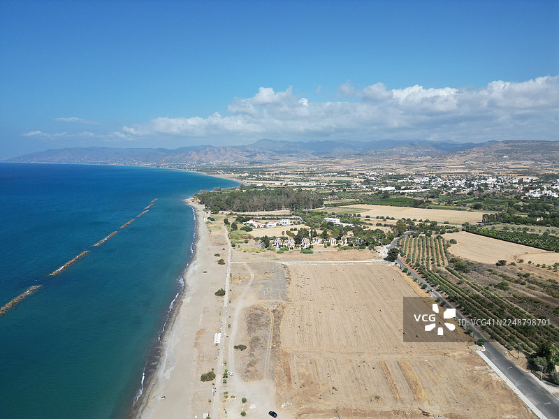 高角度航拍，俯瞰风景如画的海岸线，海滩沙软，海水深蓝，远处的城镇沐浴在晴朗的天空下。图片素材