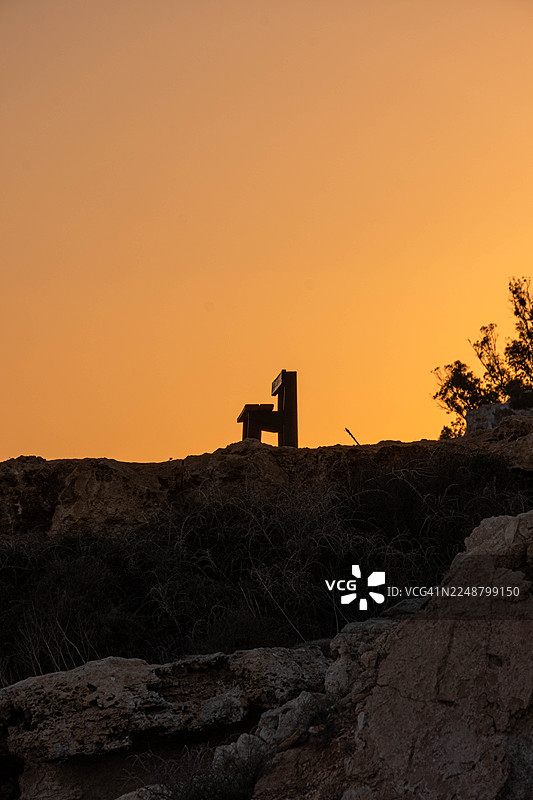 日落时分，荒凉山丘上孤独长椅的剪影，天空色彩鲜艳橙红。图片素材